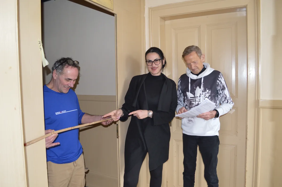 Die Wirtin und zwei Handwerker messen einen Eingang.